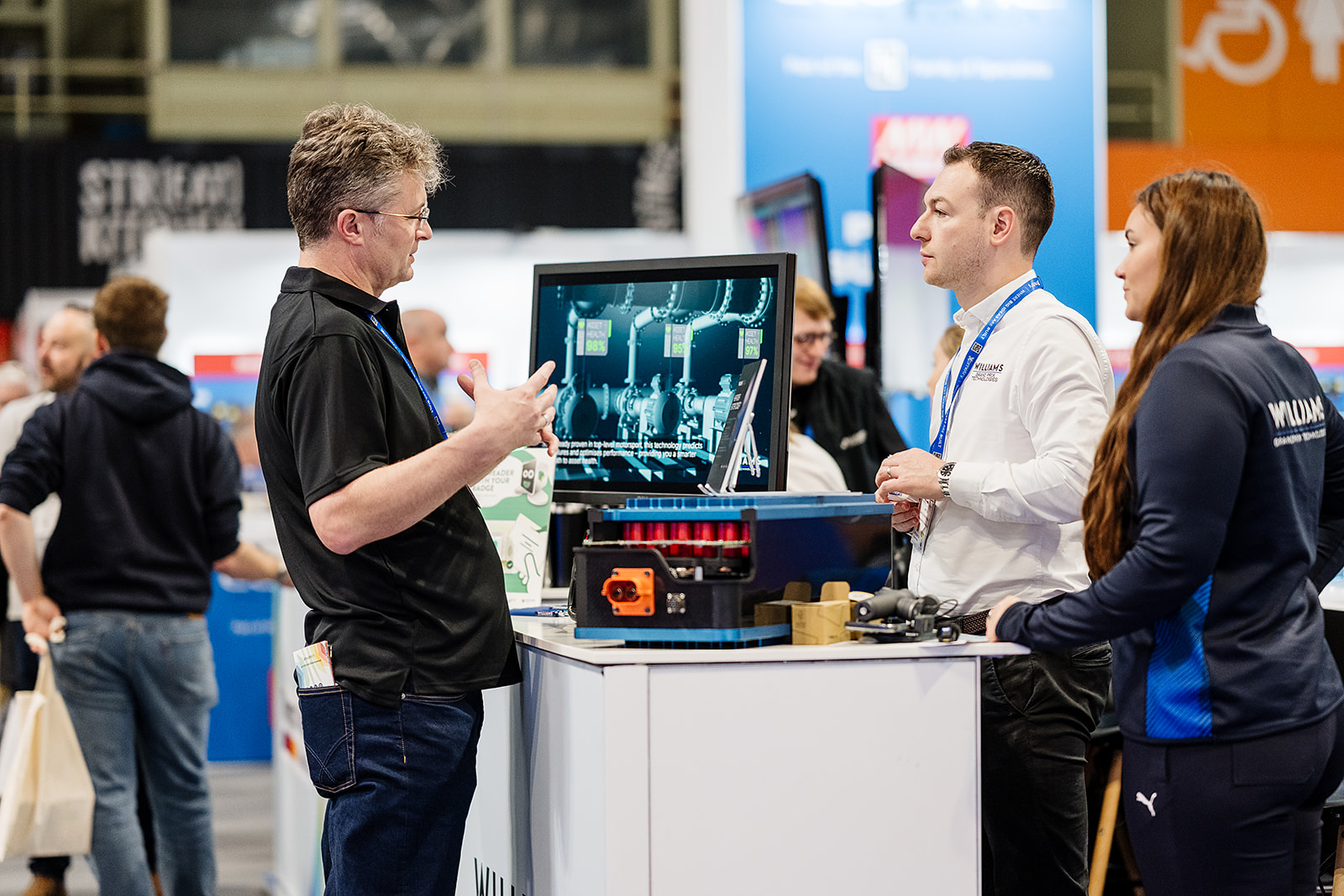 An exhibitor demonstrating an asset health monitoring display to two visitors on a stand at Advanced Engineering