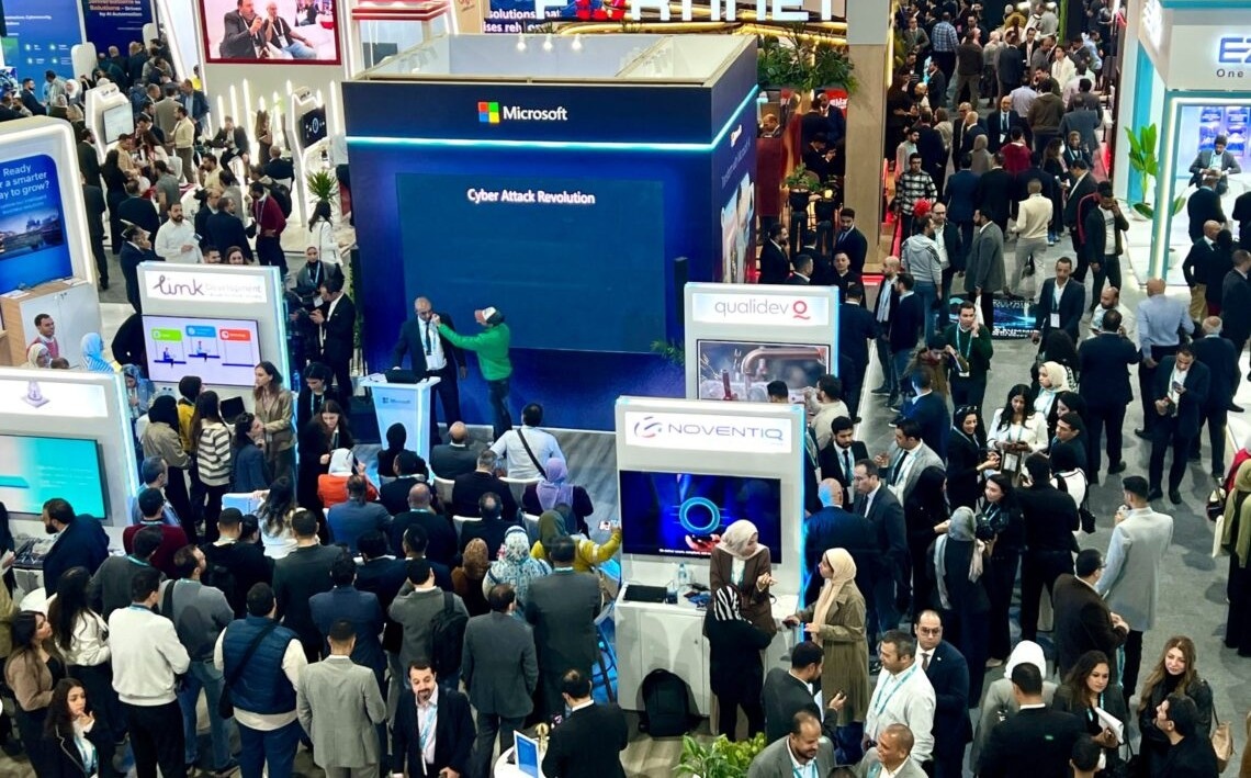Delegates gathered around exhibitor stands on the Ai Everything show floor, including a Microsoft stand with a large display screen